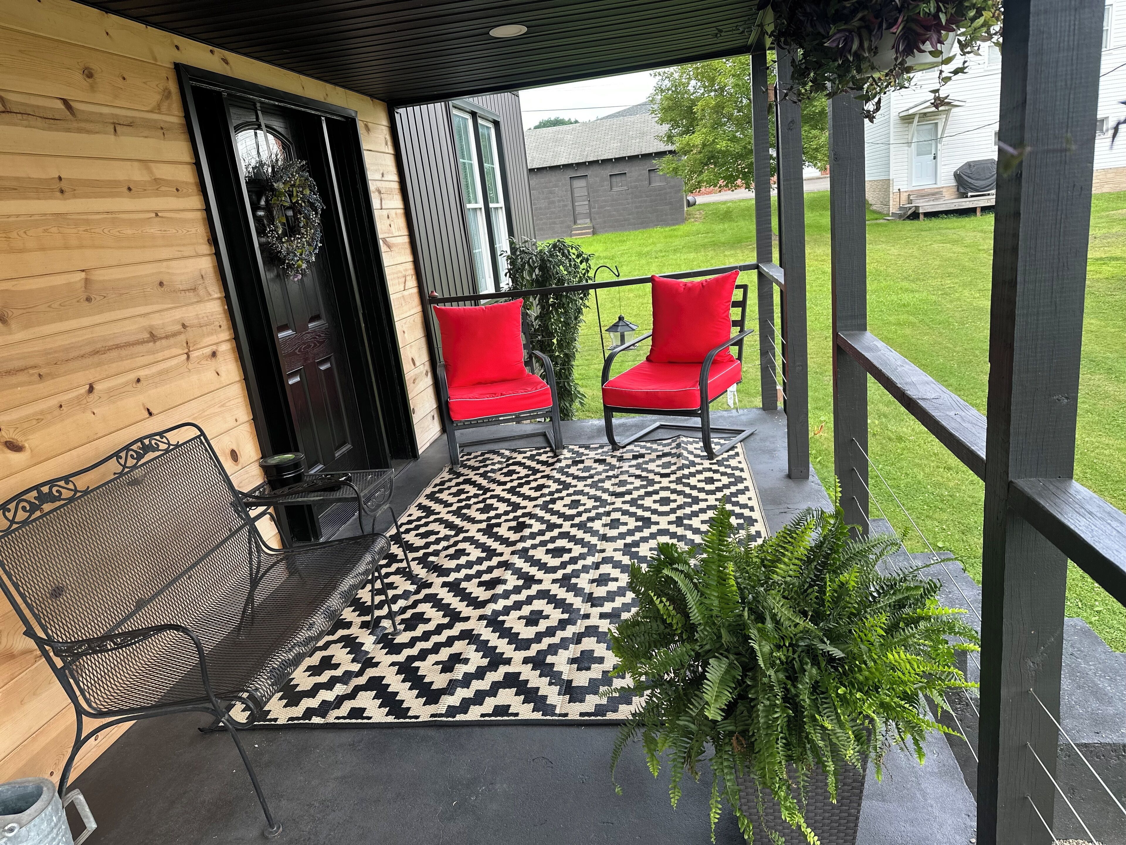 Eine überdachte Veranda mit zwei roten Stühlen und einer schwarzen Metallbank.