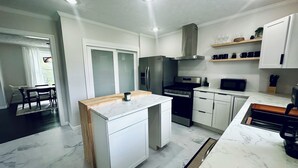 Una cocina moderna con armarios blancos, una isla central, electrodomésticos de acero inoxidable y un comedor con mesa y sillas.
