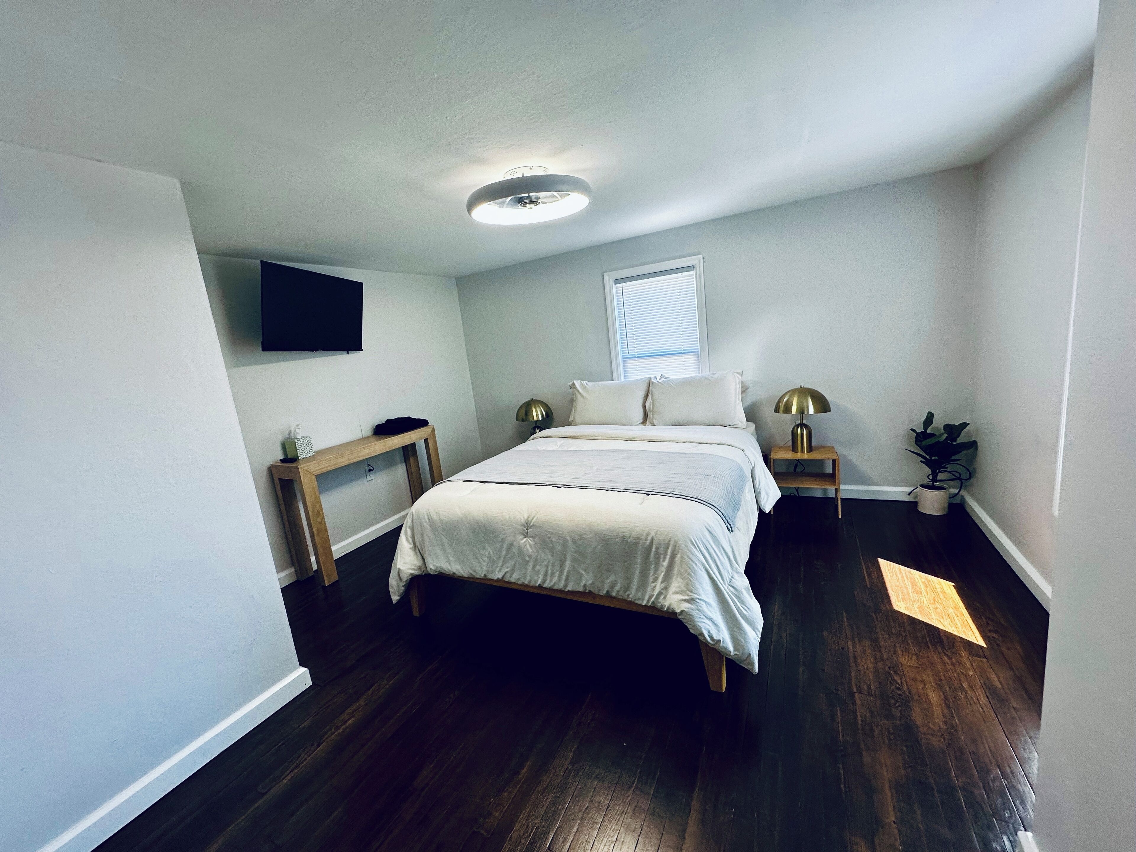 A bedroom with a bed, bedside tables, a lamp, a TV, a window, and a ceiling light.