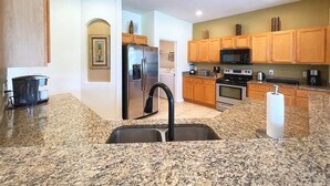 Eine Küche mit Granit Arbeitsplatten, Edelstahlgeräten, Holzschränken und einem schwarzen Wasserhahn.