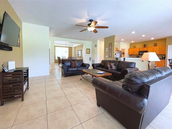 A spacious living room with a large flat-screen TV, leather sofas, a coffee table, and a ceiling fan.