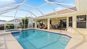 Piscina com estrutura de vidro, cadeiras de espreguiçadeira e área de estar com móveis de exterior.