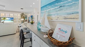 Cocina moderna con un cuadro grande de una escena de playa, un modelo de velero y una guía de bienvenida sobre la encimera.