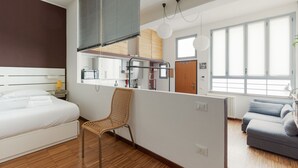A modern hotel room with a large bed, a chair, a kitchenette, and a view of the city. - GuestHost - Milano Bovisa Apartment (Milano)