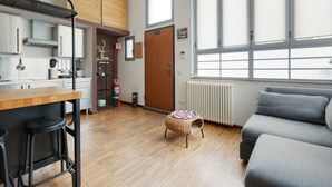 A modern kitchen with a wooden countertop, a dining area with stools, a sofa, and a window with blinds. - GuestHost - Milano Bovisa Apartment (Milano)