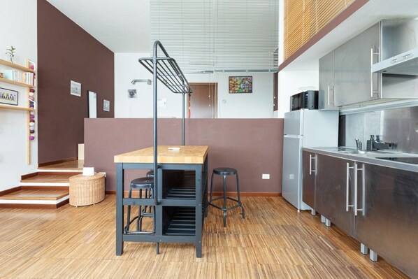 A modern kitchen with a wooden table, black stools, and stainless steel appliances.