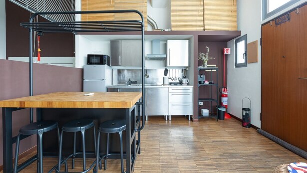 A compact kitchen with a wooden table and bar stools, a microwave, and a sink. - GuestHost - Milano Bovisa Apartment (Milano)