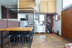 A compact kitchen with a wooden table and bar stools, a microwave, and a sink.