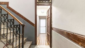 A narrow hallway with a wooden staircase on the left, a patterned floor, and a door at the end. - GuestHost - Cozy 86 sqm apartment, able to accommodate up to 6 people, located on the mezzanine floor of a characteristic building (steps to access). The property is located in a strategic position, a few steps from the famous Catacombs of the Capuchins  (Palermo)