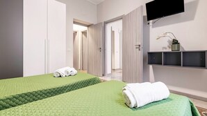 A hotel room with two beds, a TV, a plant, and a view of the hallway. - GuestHost - Cozy 86 sqm apartment, able to accommodate up to 6 people, located on the mezzanine floor of a characteristic building (steps to access). The property is located in a strategic position, a few steps from the famous Catacombs of the Capuchins  (Palermo)