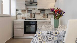 A compact kitchen with a gas stove, oven, and modern cabinetry. A dining table with a patterned tablecloth is visible. - GuestHost - Cozy 86 sqm apartment, able to accommodate up to 6 people, located on the mezzanine floor of a characteristic building (steps to access). The property is located in a strategic position, a few steps from the famous Catacombs of the Capuchins  (Palermo)