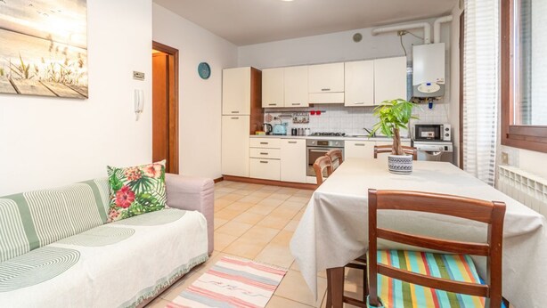 Une cuisine compacte avec des meubles blancs, une table à manger avec une chaise, un canapé avec un coussin, une horloge et un radiateur.