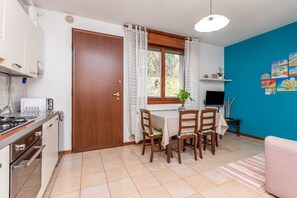 Una cocina equipada con estufa, horno y microondas. Hay una mesa de comedor con sillas y un televisor. Una puerta da a un espacio exterior.