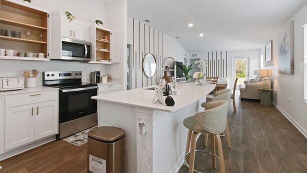 Une cuisine moderne avec des meubles blancs, des appareils en acier inoxydable et un îlot central doté de tabourets de bar.