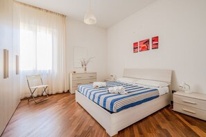 A modern bedroom with a bed, bedside tables, a chair, and artwork on the wall. - GuestHost - Sweet Home - Cozy apartment in La Spezia (La Spezia)
