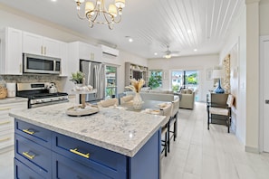 A modern kitchen with white cabinets, a large island, and a dining area with a sofa and chairs. - Pineapple Premier Villa (3 Bedroom), Waterfront Bliss with boat access, Kayaks, Sandbar in the Baham (Nassau)