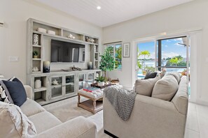 A modern living room with a sofa, a coffee table, and a TV stand with shelves. - Pineapple Premier Villa (3 Bedroom), Waterfront Bliss with boat access, Kayaks, Sandbar in the Baham (Nassau)