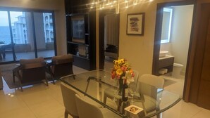 Uma sala de estar moderna com uma mesa de jantar de vidro, assentos confortáveis, uma TV e uma varanda com vista para o mar.