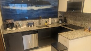 Cozinha moderna com bancada de granito, eletrodomésticos de aço inoxidável e uma grande janela com vista para o oceano.