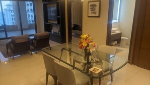 Uma área de refeições moderna com mesa de vidro, cadeiras, um vaso de flores e uma garrafa de vinho.