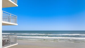 Vista a la playa desde un balcón, con cielo despejado y olas del océano.