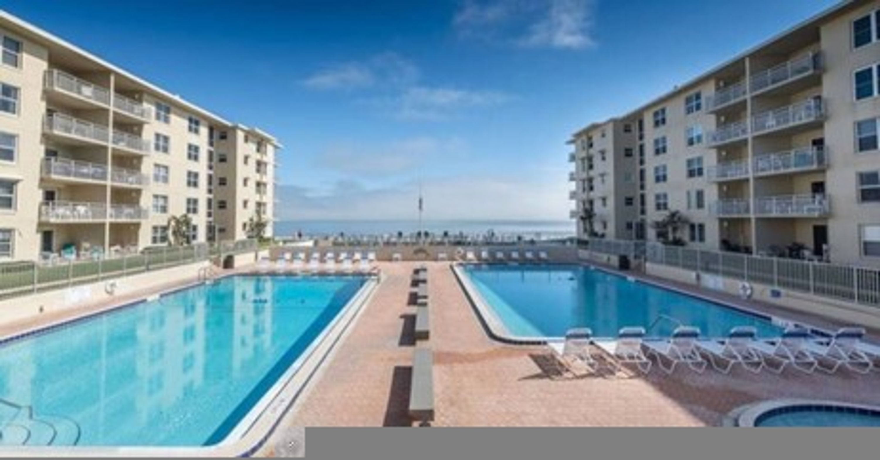 A swimming pool area with two pools, lounge chairs, and a view of the ocean.