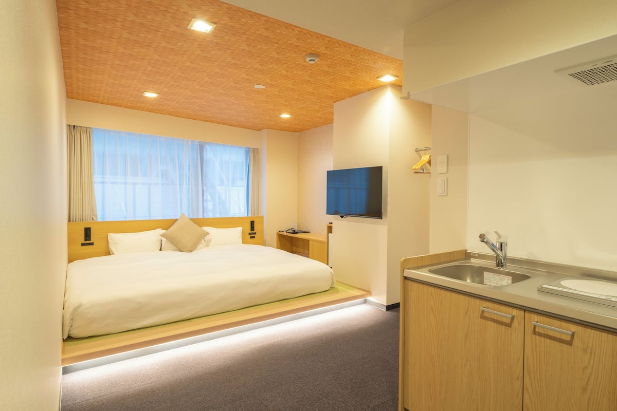 A hotel room with a bed, a TV, a sink, and a wooden cabinet.