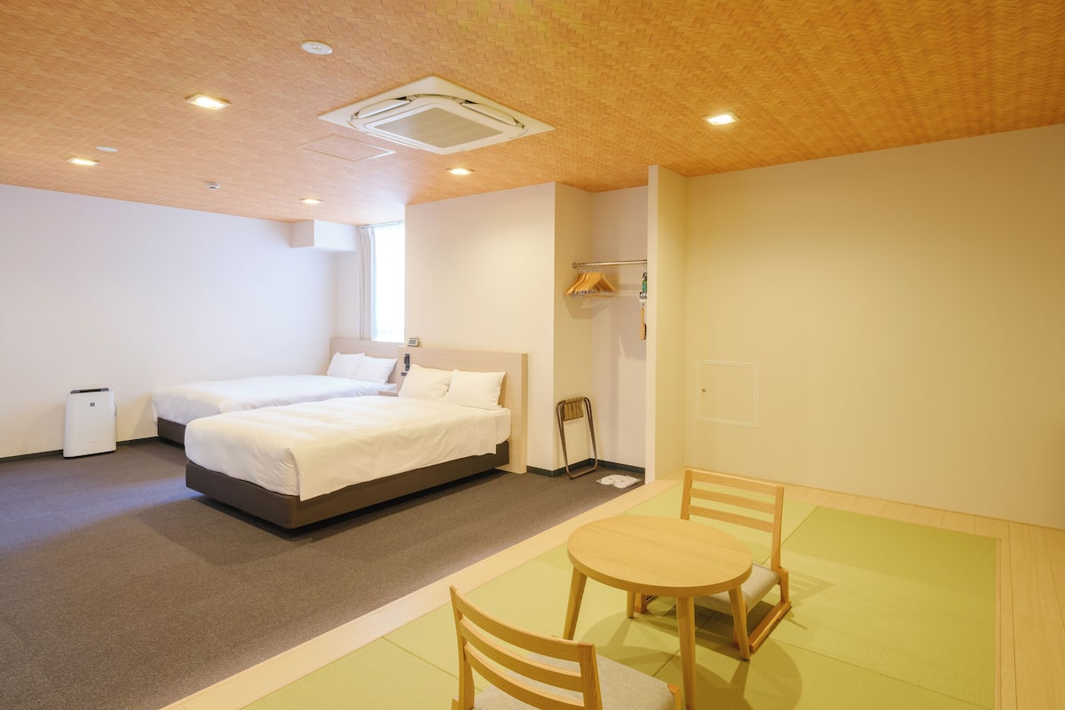 A hotel room with a bed, a small table with chairs, a radiator, and a window.