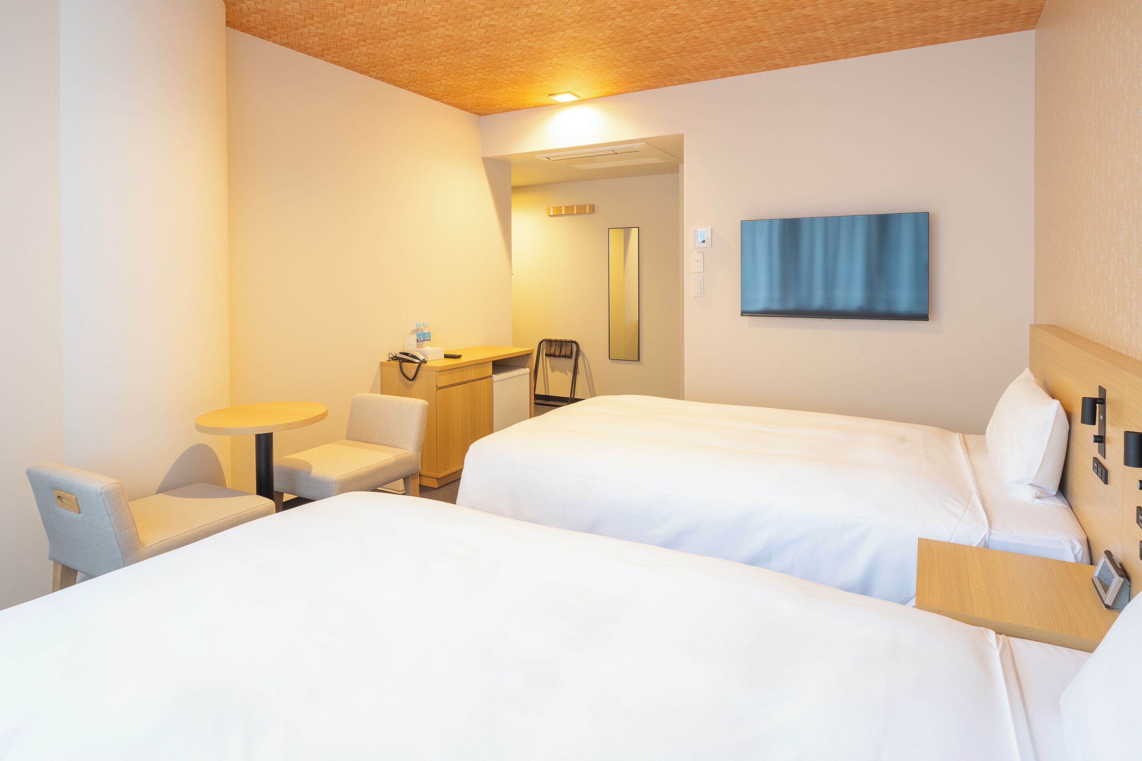 A hotel room with two beds, a desk, a chair, a small table, and a mirror.
