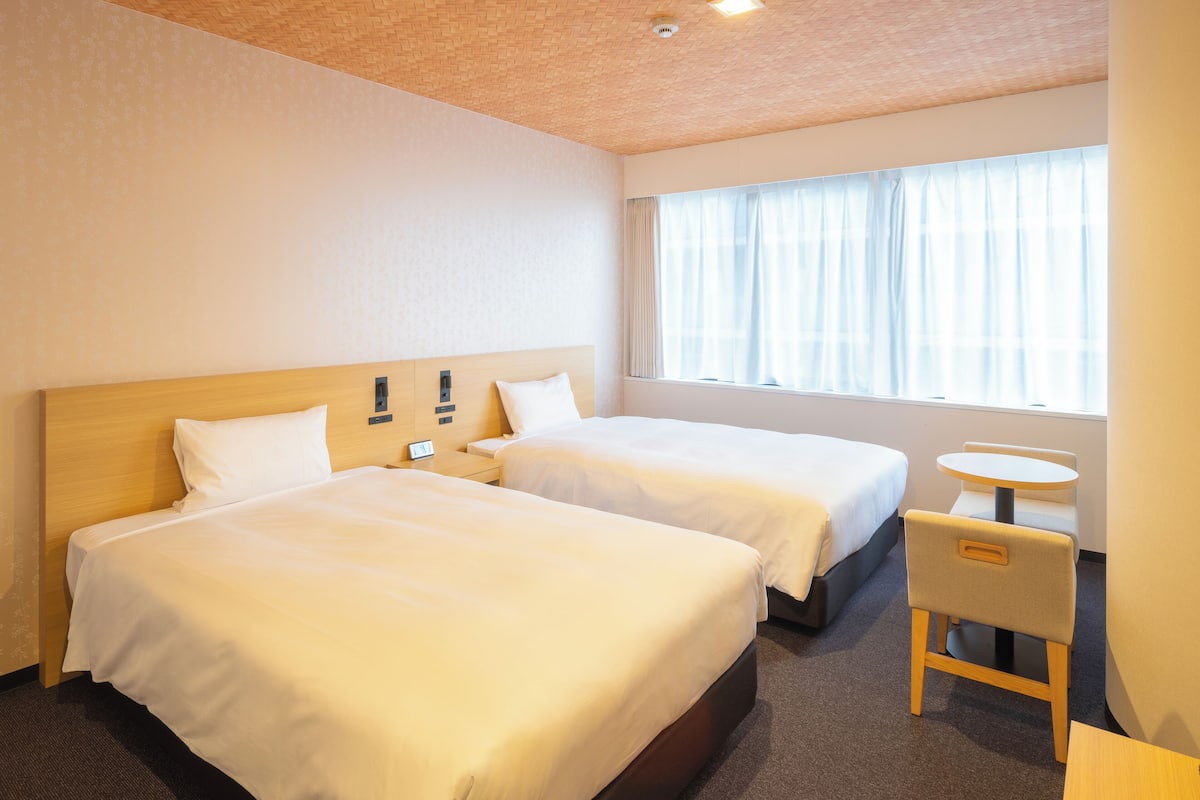 A hotel room with two beds, a small table, and a chair.