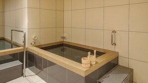 Un moderno espacio de spa con un jacuzzi de paredes de vidrio, escalones de madera y un panel de control.