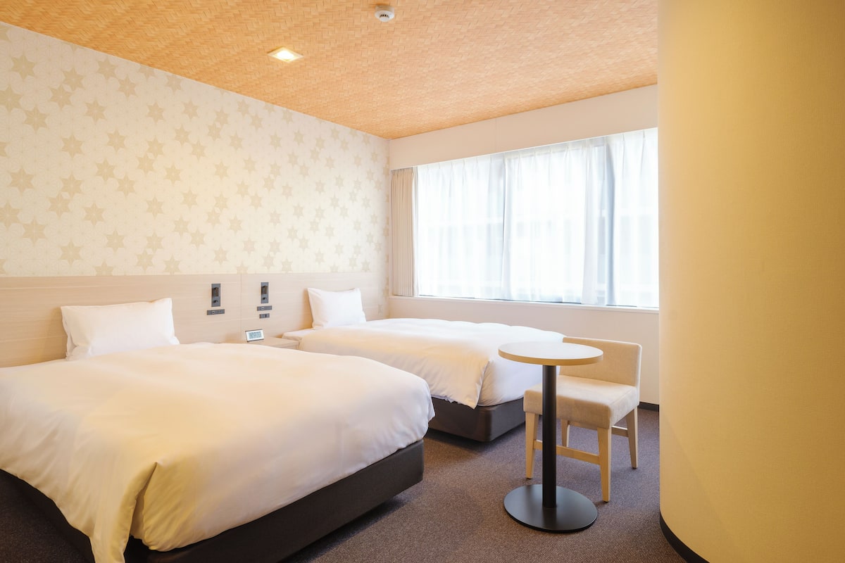 A hotel room with two beds, a round table, and a window with curtains.