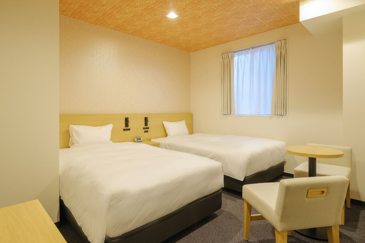 A hotel room with two beds, a small round table, and a chair.
