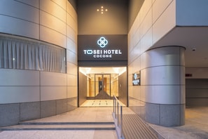 La entrada al Hotel Tosei Cocone, con un diseño moderno, presenta un llamativo letrero iluminado y un frente de vidrio.