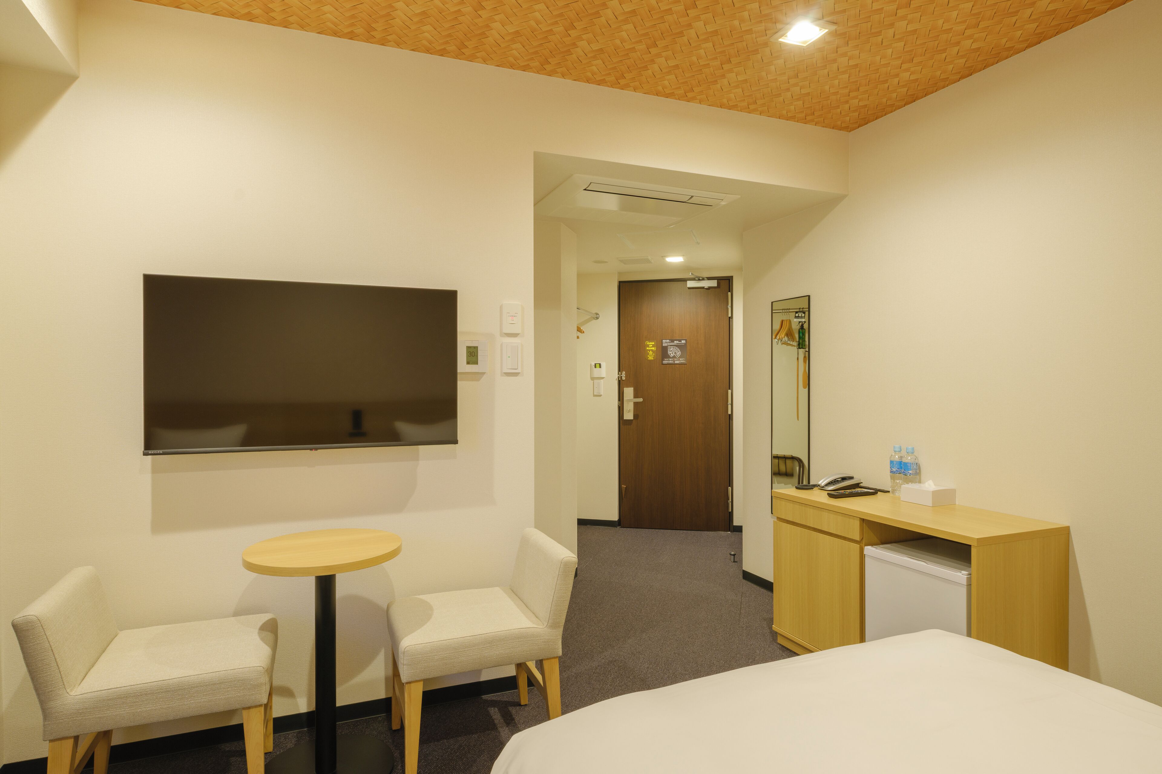 A hotel room with a bed, a desk, a chair, a small table, and a TV.