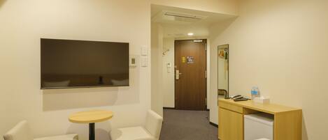 A hotel room with a bed, a desk, a chair, a small table, and a TV.