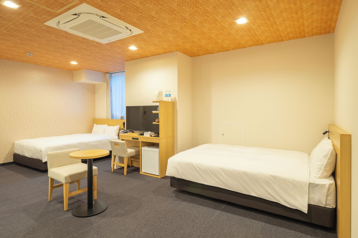 A hotel room with two single beds, a desk with a chair, a small table, and a TV.