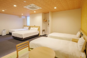 Habitación de hotel con dos camas, una mesita y una silla. Hay una ventana con cortinas, un radiador y una estantería con objetos.