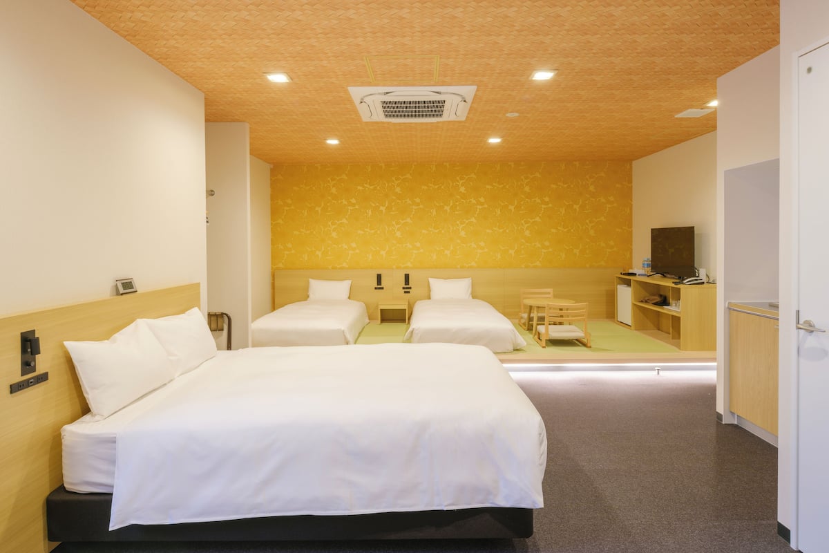 A hotel room with two beds, a wooden ceiling, a small desk, a television, and a minibar.