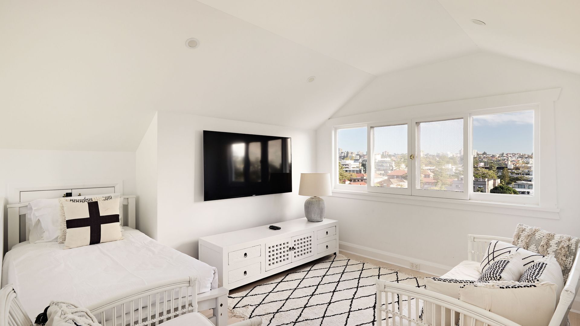Un dormitorio con cama, televisión, ventana con vista a la ciudad, mesita de noche y cuna.