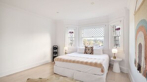 Une chambre à coucher comprenant un lit, deux tables de chevet, un radiateur et des fenêtres ornées de grilles décoratives.