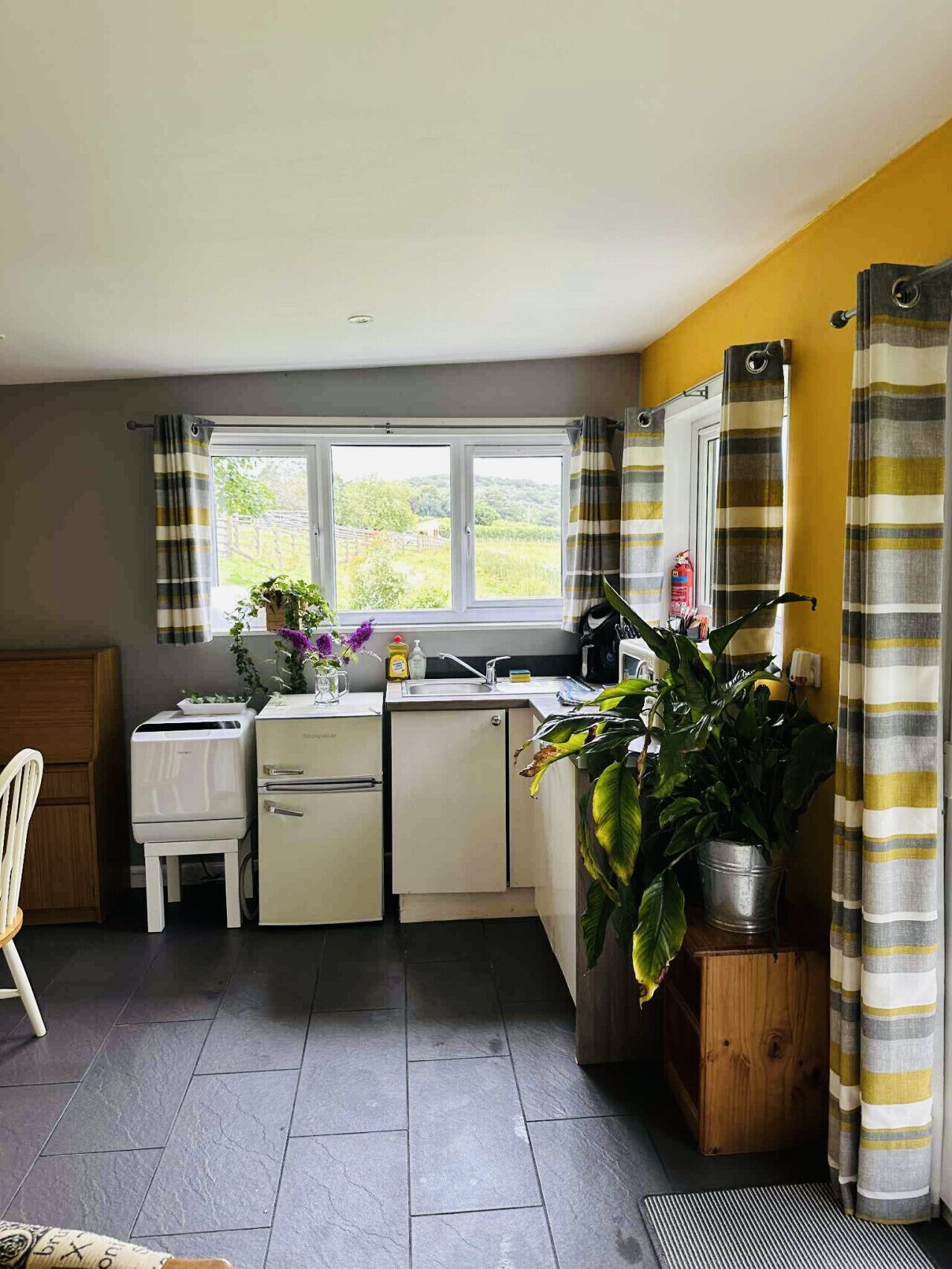 A compact kitchen with a window, a refrigerator, a sink, and a dining area with a chair.