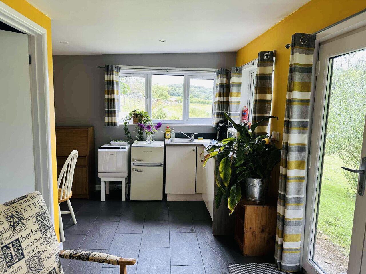 A compact kitchen with a window, a refrigerator, a sink, and a chair.