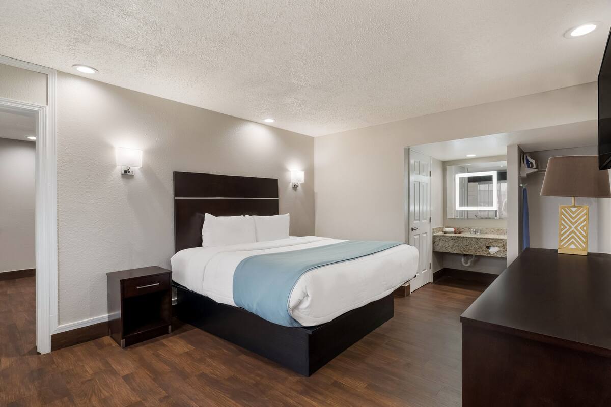 Una habitación de hotel moderna con una cama grande, mesitas de noche, un escritorio y un baño visible a través de una puerta abierta.