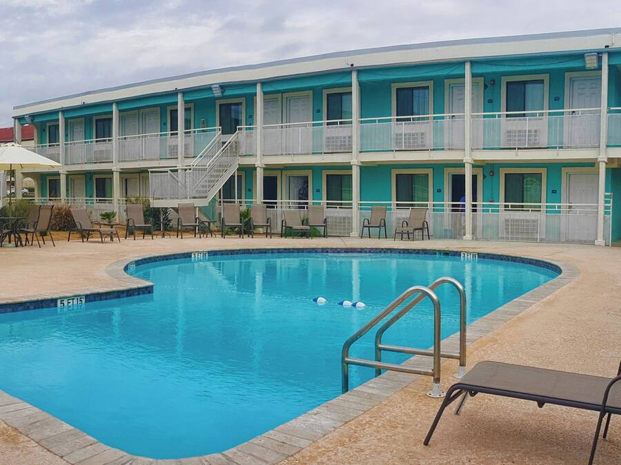 Un hotel amb piscina, zona d'estar a l'aire lliure i un edifici de diversos pisos amb balcons.