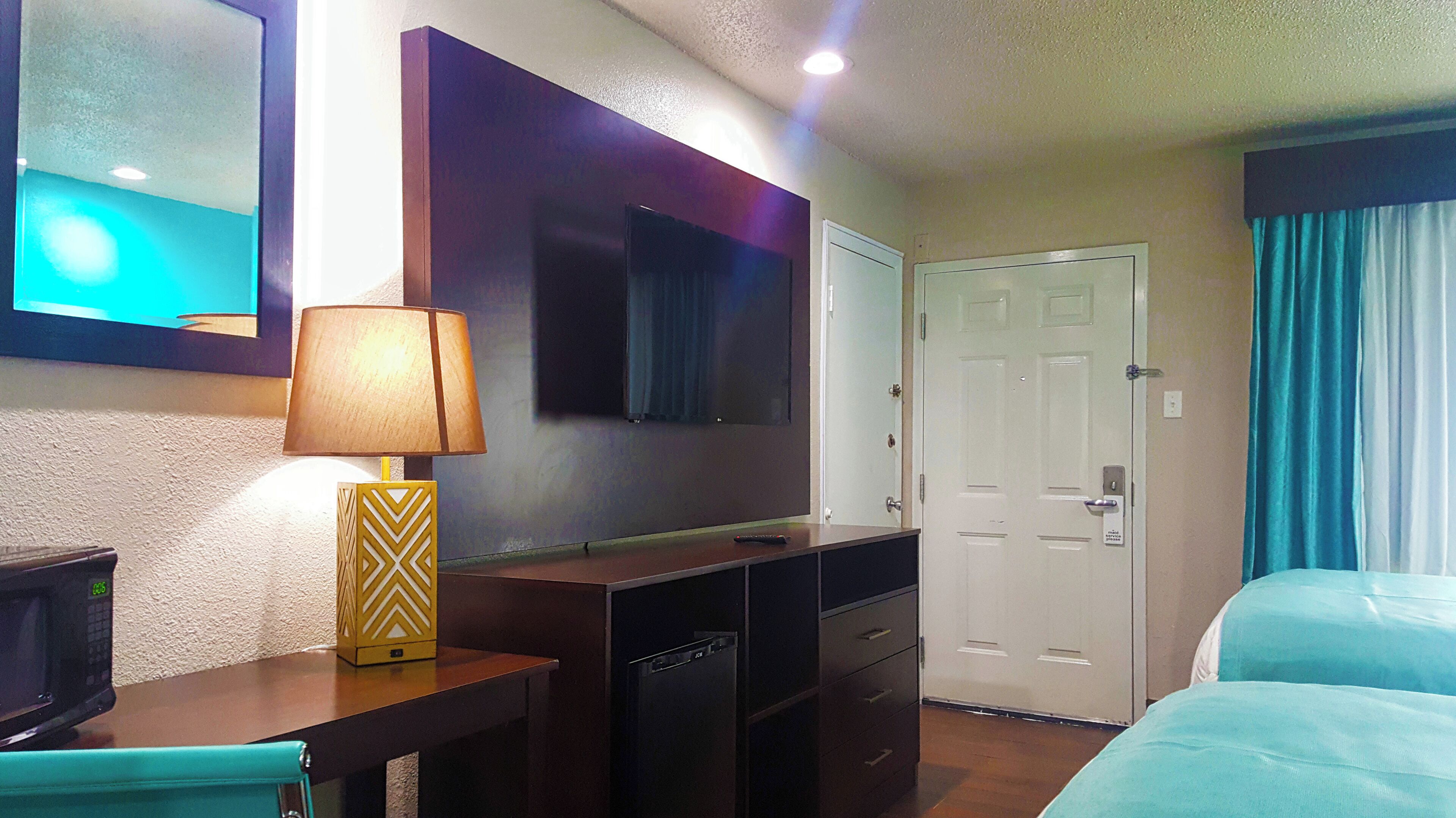 A hotel room with a bed, a desk with a lamp, a TV, and a door.