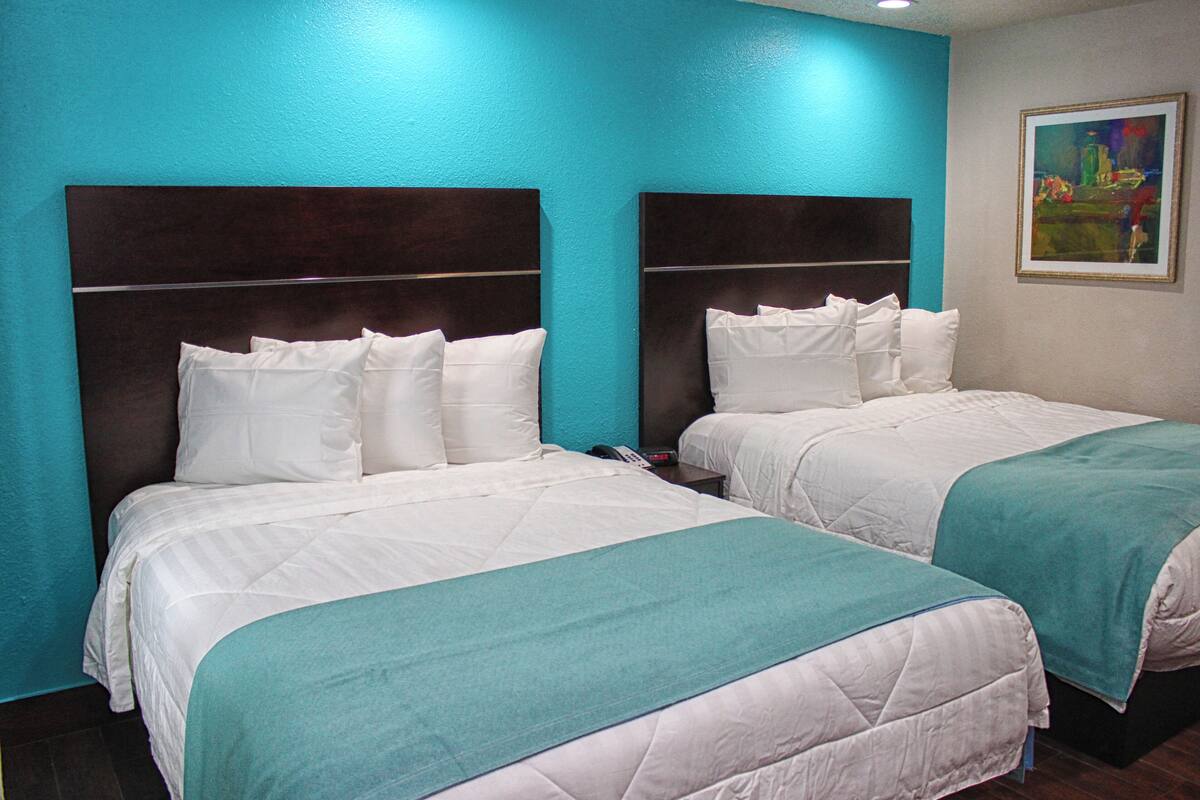 Habitación de hotel con dos camas, paredes color aguamarina y un cuadro en la pared.