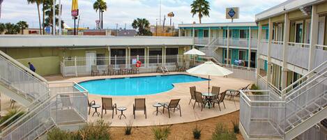 A hotel with a swimming pool, outdoor seating, and a view of the surrounding area including palm trees and a McDonald's sign.