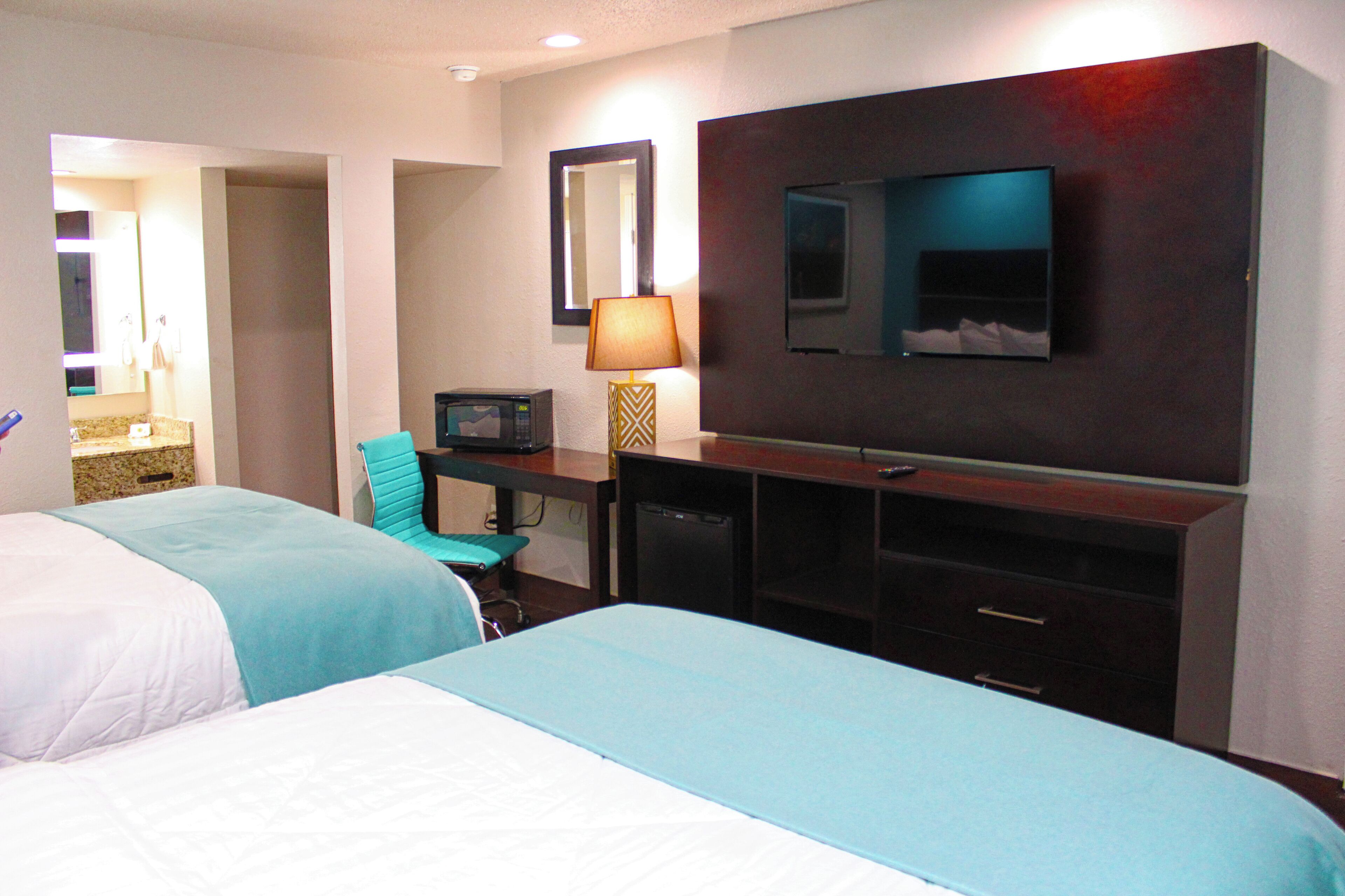 Habitación de hotel con dos camas, un escritorio con lámpara, televisión y espejo.