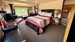 Un dormitorio con cama, escritorio, sillón, chimenea y vistas al exterior.